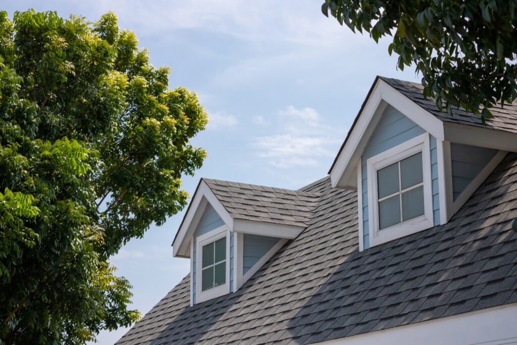 Roof shingles with garret house on top of the house among a lot of trees. dark asphalt tiles on the roof background